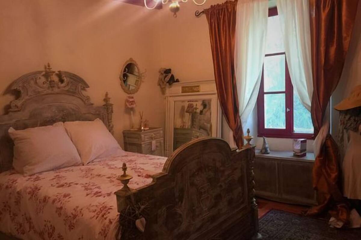 A bedroom with a large bed, a dresser, a mirror, and a window with curtains.