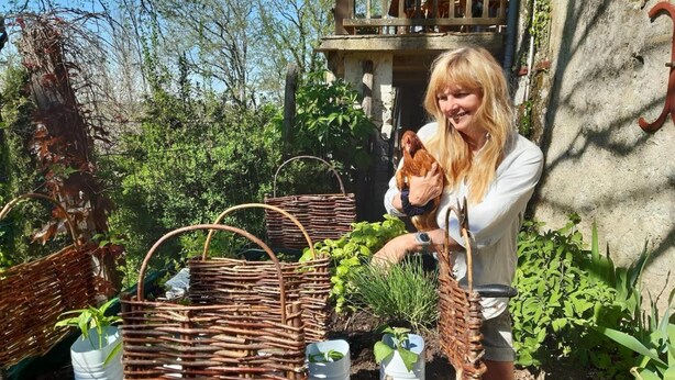 A person holding a chicken near a garden with wicker baskets and potted plants. - Le Peyrail (Les Lèves-et-Thoumeyragues)