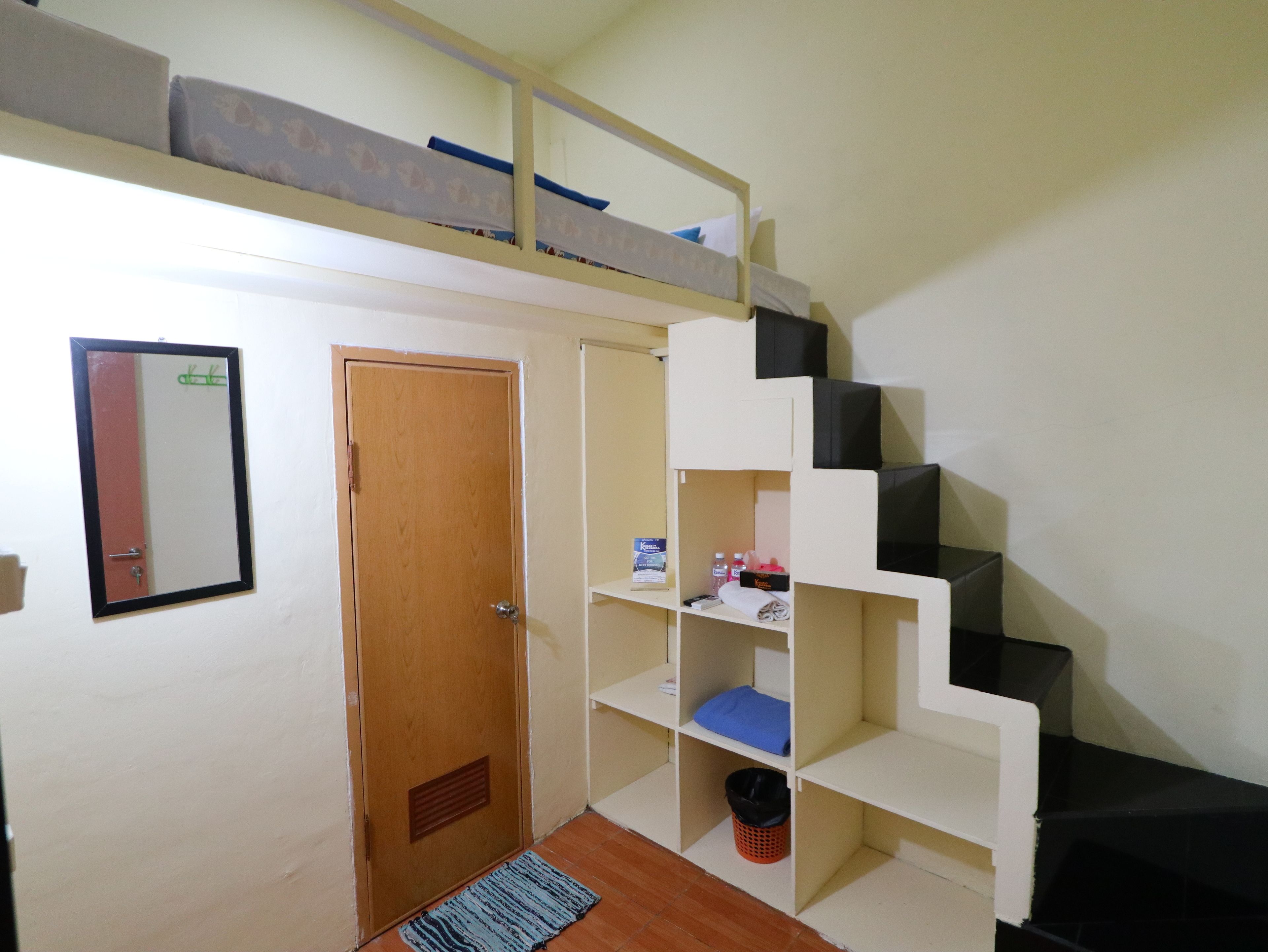 A room with a bunk bed, a door, a mirror, and a small shelving unit with various items.