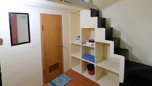 Een kamer met een stapelbed, een deur, een spiegel en een klein rek met diverse spullen.