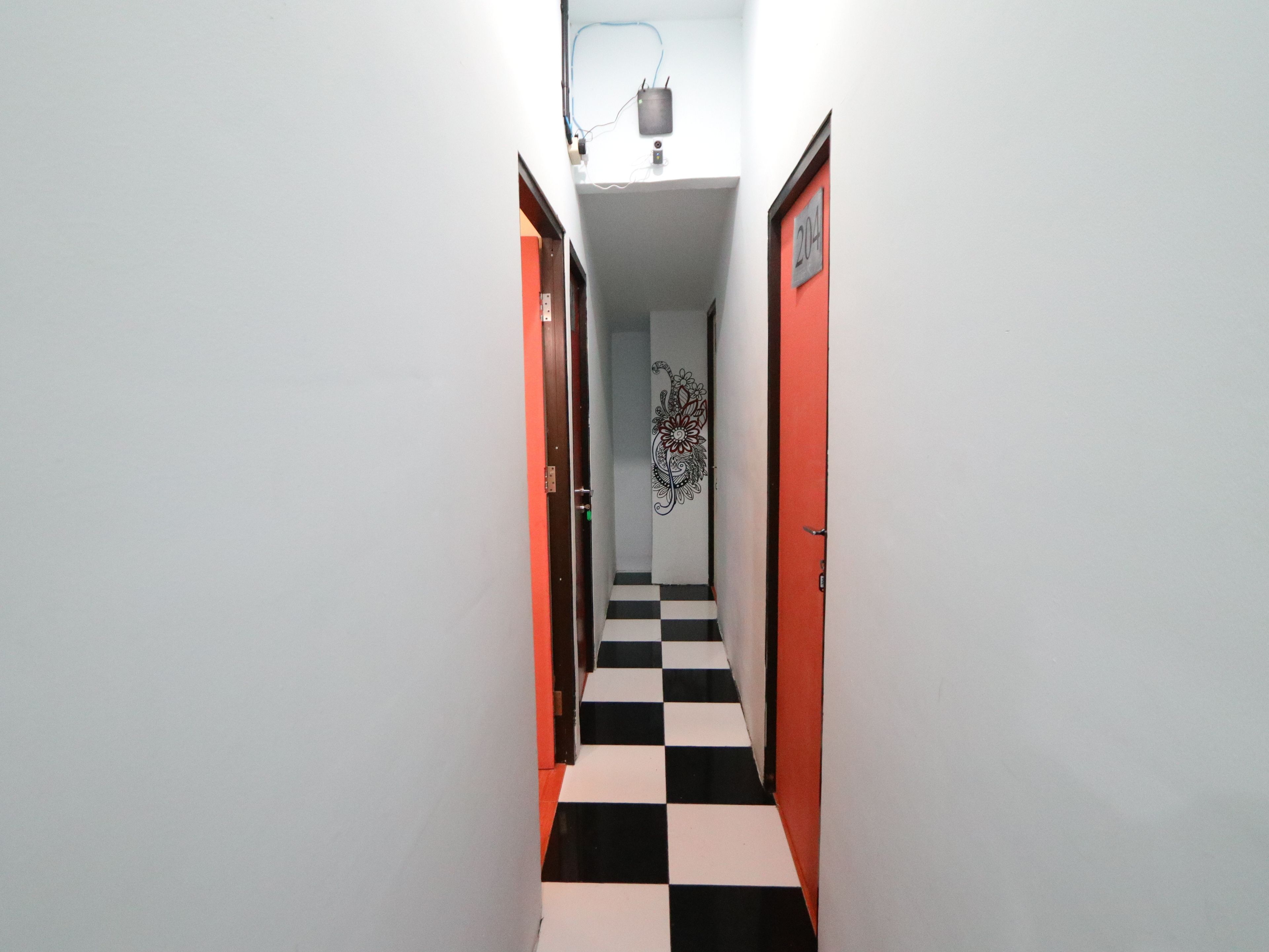 A narrow hallway with a checkered floor, white walls, and two doors, one with a red frame and the other with a black frame.