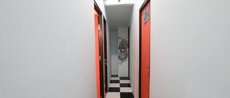 A narrow hallway with a checkered floor, white walls, and two doors, one with a red frame and the other with a black frame.