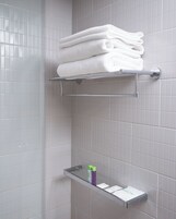 Un baño con paredes de azulejos blancos, un perchero con toallas dobladas y un estante con artículos de aseo.