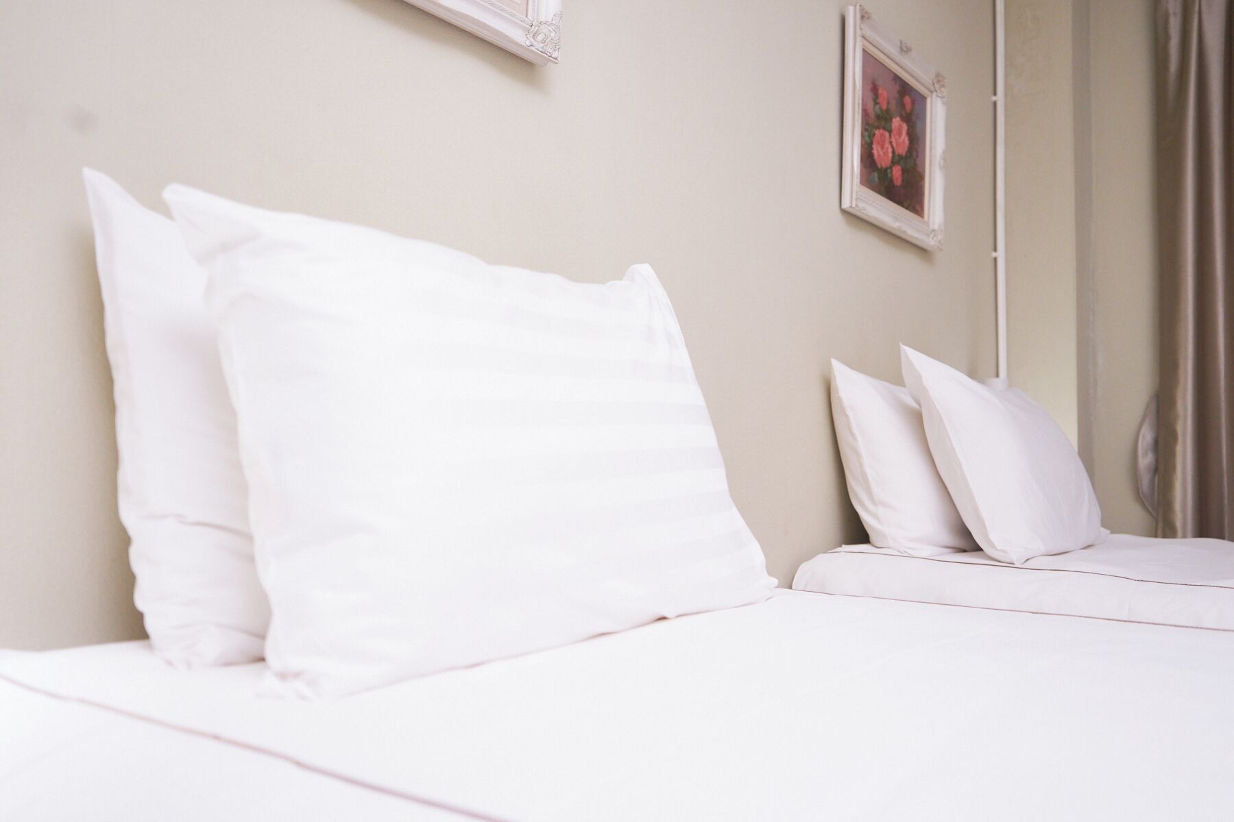 A neatly made bed with white linens and pillows, a framed picture on the wall, and a window with curtains.