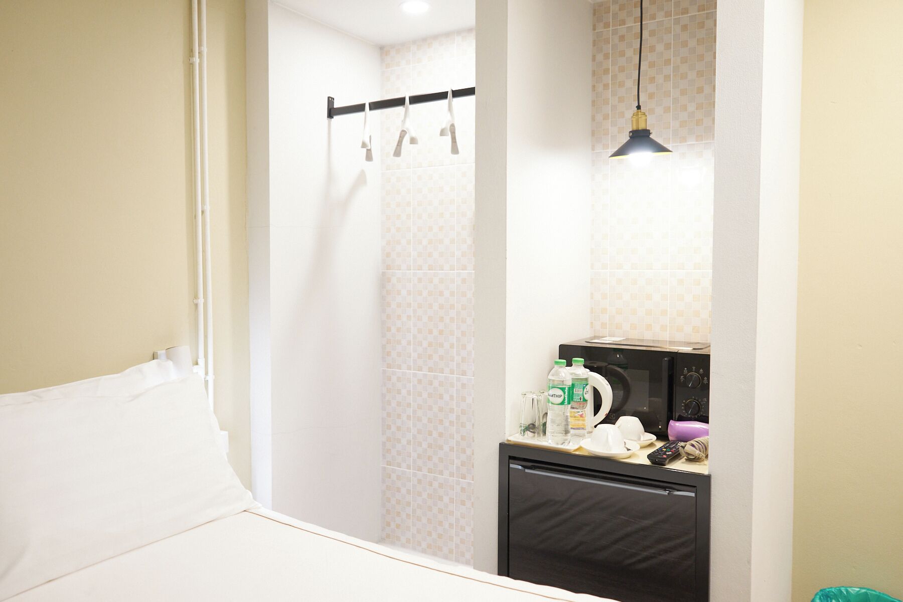 Habitación de hotel pequeña con cama, zona de ducha, kitchenette con microondas y lámpara colgante.