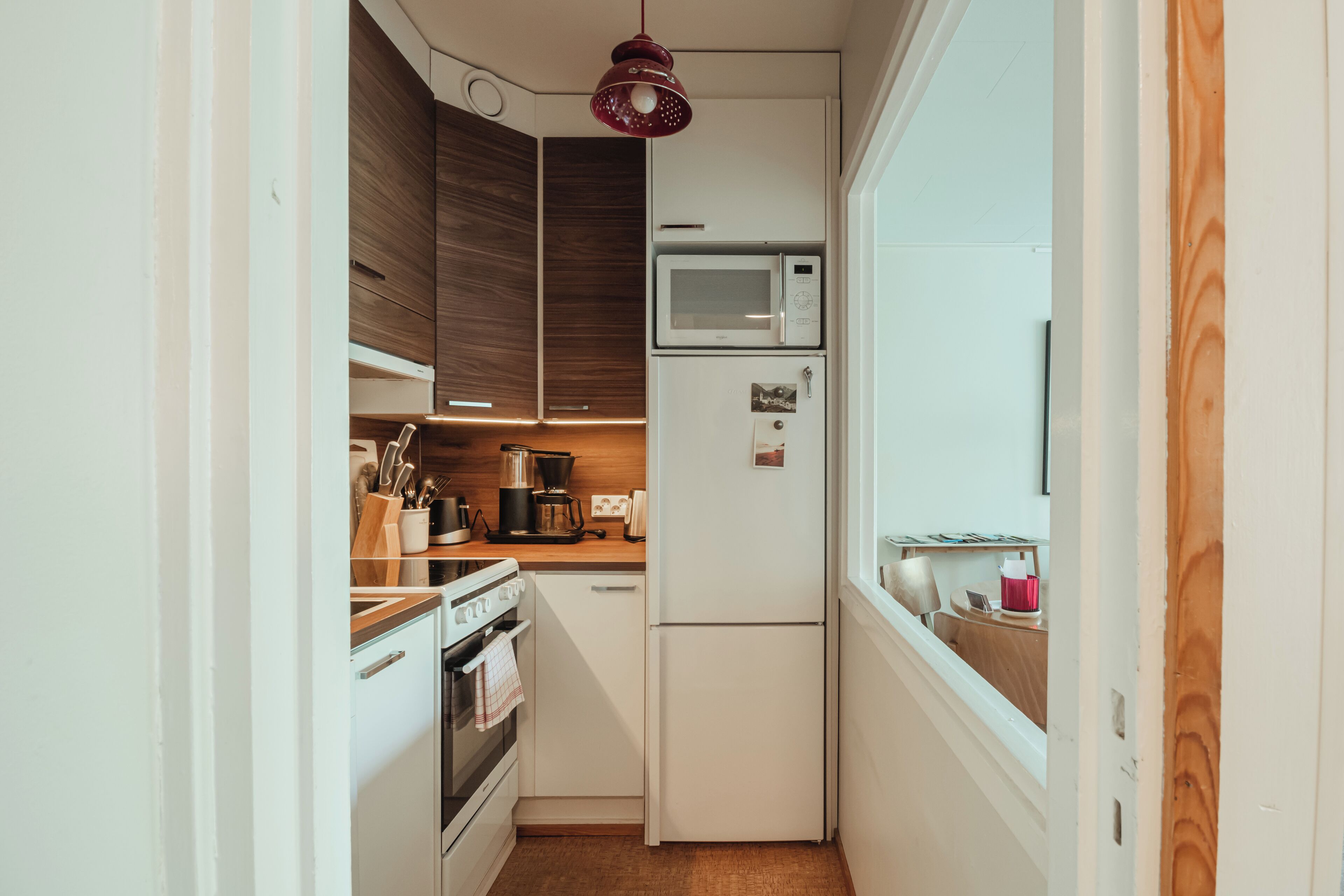 Cocina compacta con armarios blancos, microondas, refrigerador y encimera de madera.