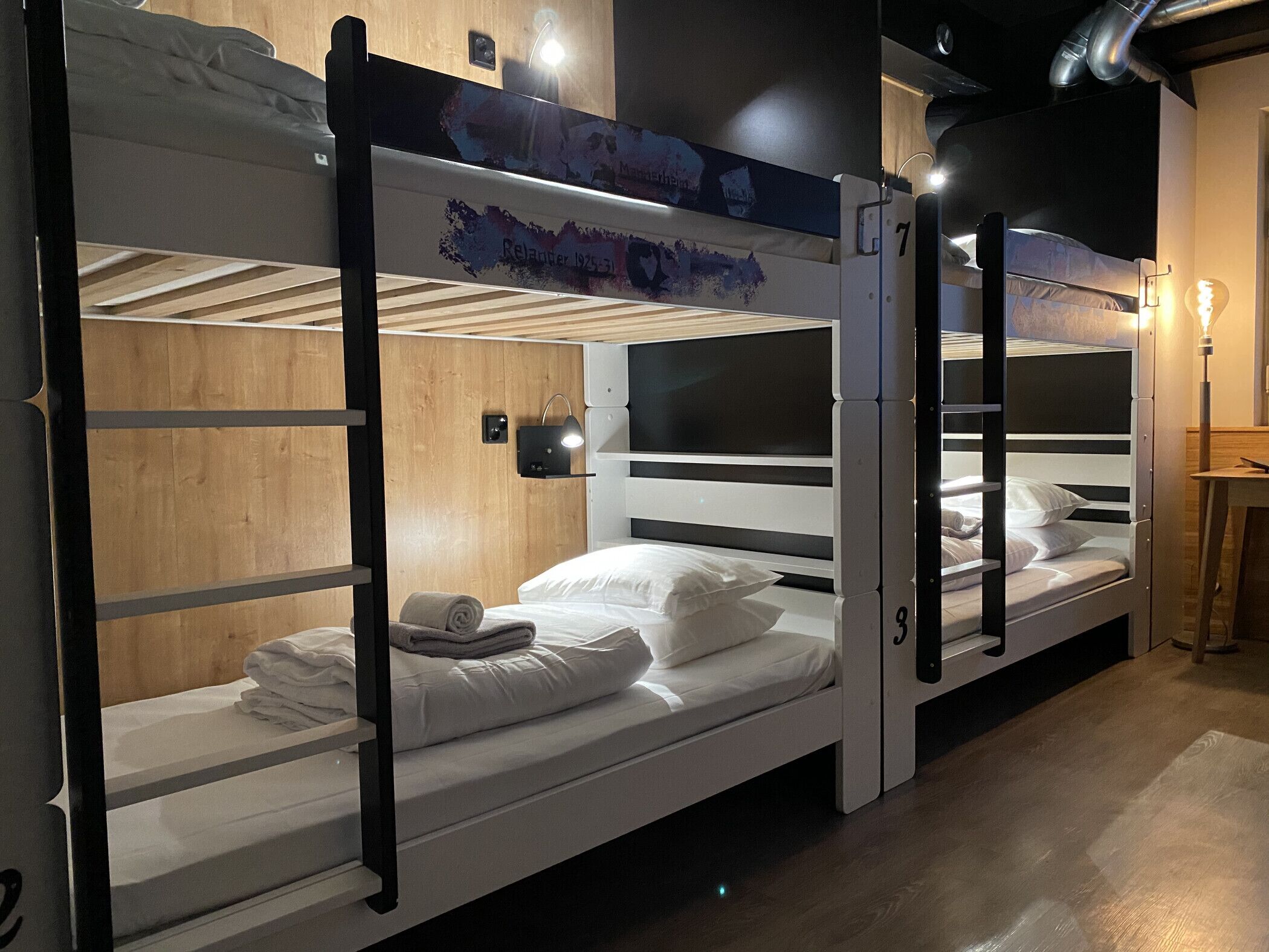 A bunk bed room with wooden walls, a small shelf, and a wall-mounted light.