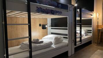 A bunk bed room with wooden walls, a small shelf, and a wall-mounted light.
