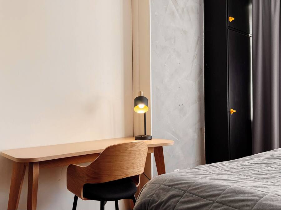 Un dormitorio con escritorio de madera, una silla, una cama con cubrecama acolchado, una mesita de noche y un tocador.