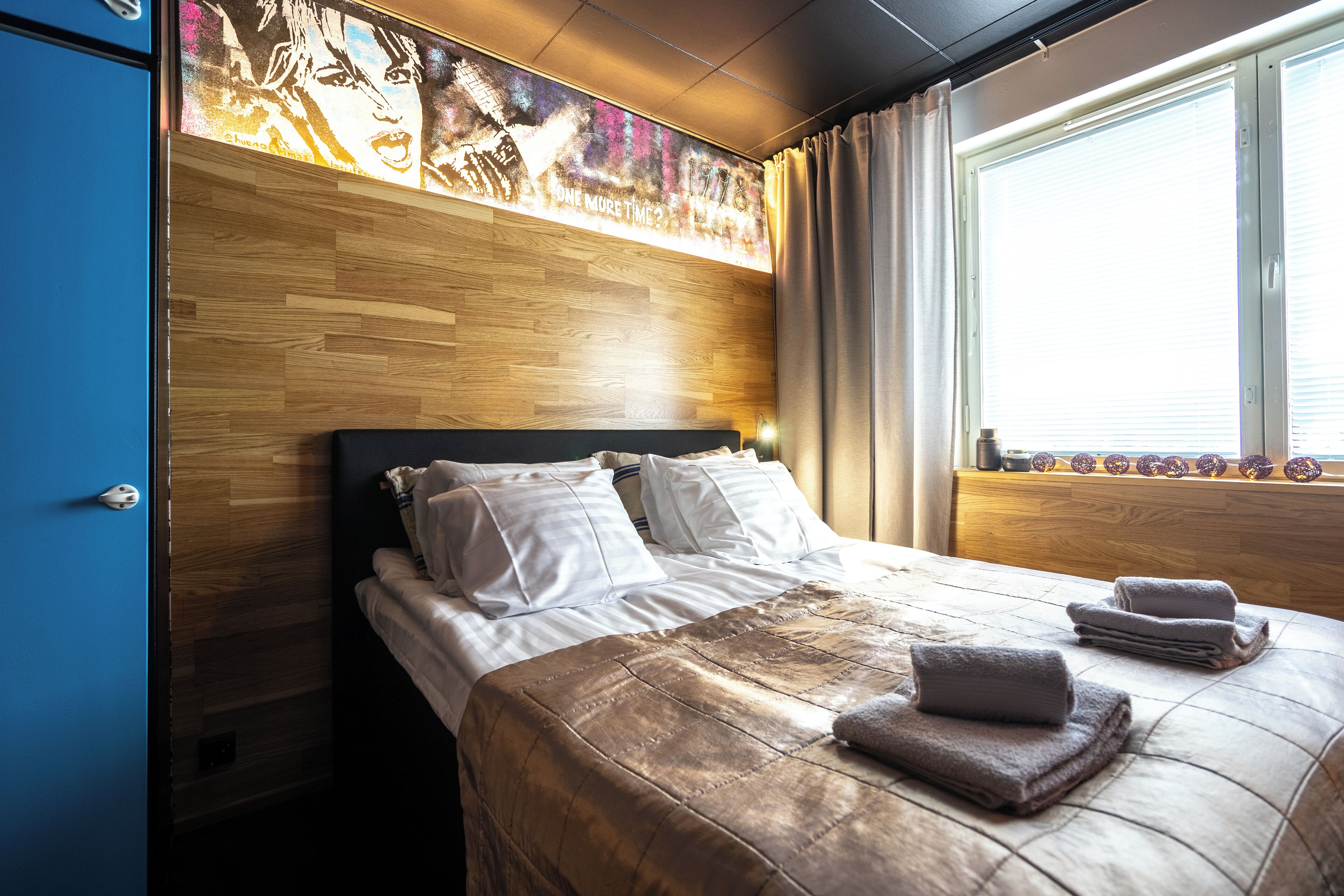 Ein Hotelzimmer mit einem hölzernen Kopfteil, einem großen Bett mit weißen Bettwäsche und einem Fenster mit Vorhängen.