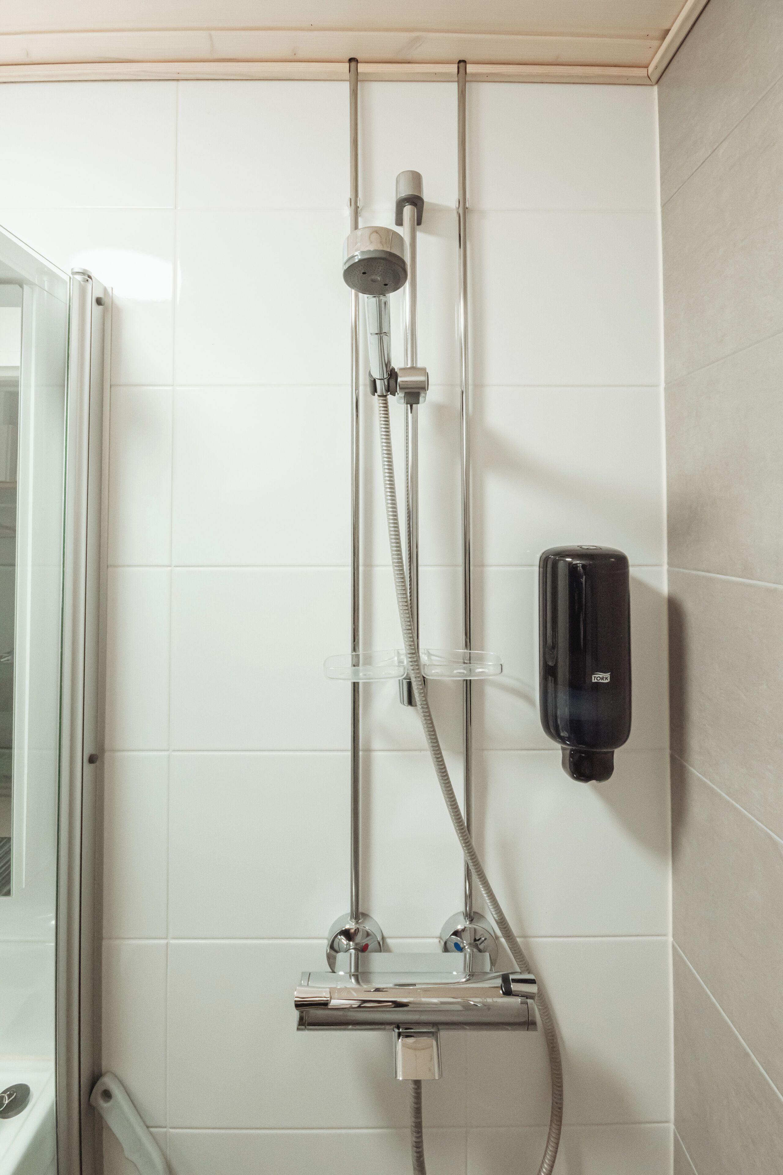 A shower with a handheld showerhead, a handheld soap dispenser, and a glass shower tray.