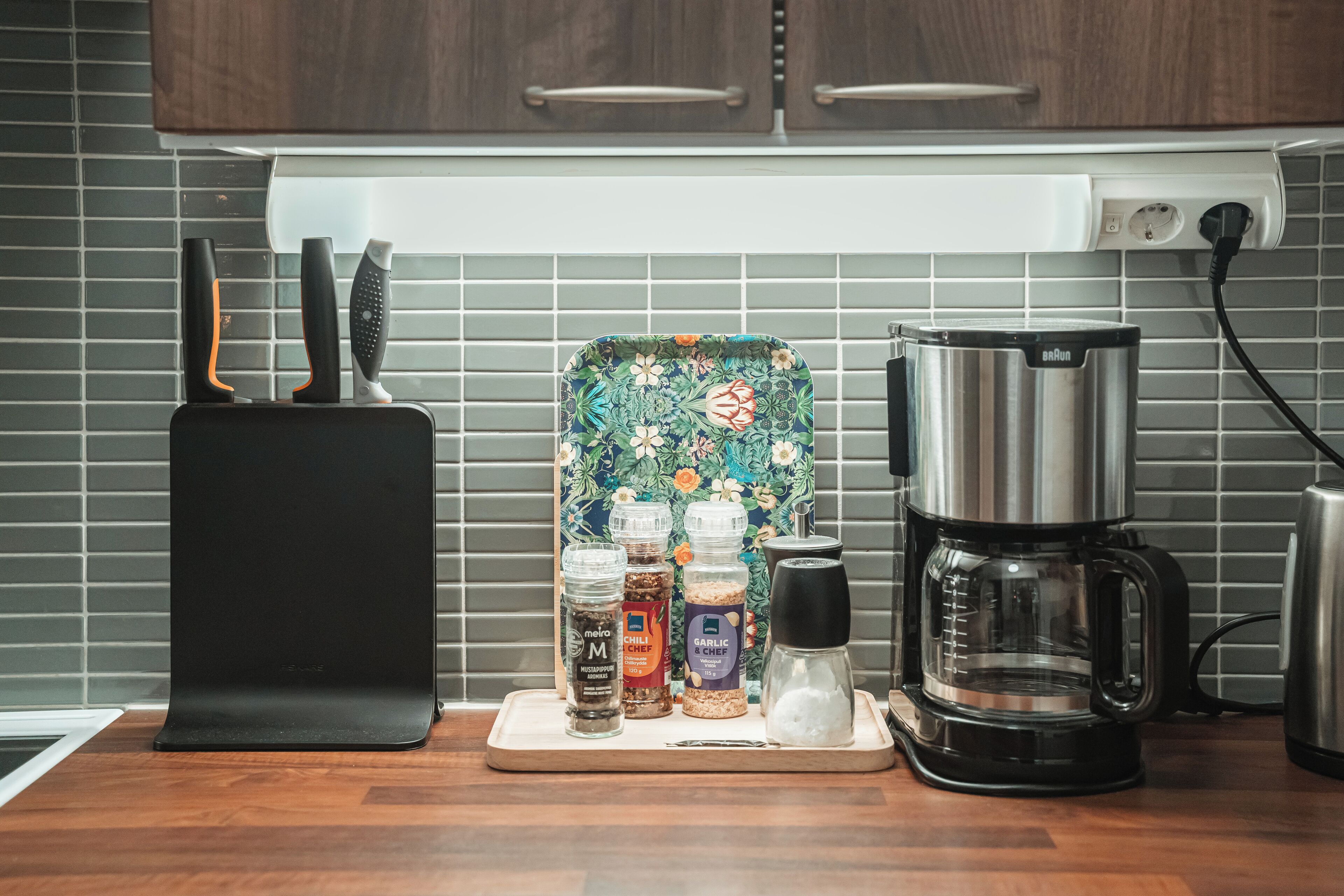 Una encimera de cocina con una cafetera, un bloque de cuchillos y frascos de especias.