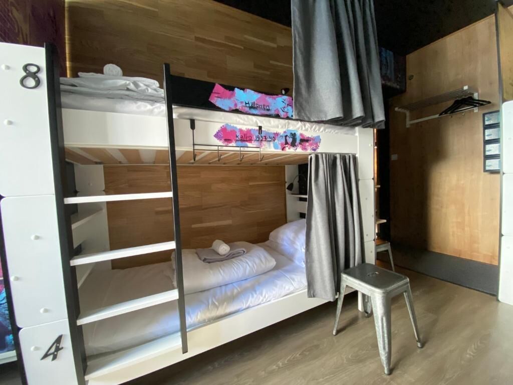 A bunk bed room with a wooden floor, a small stool, and a curtain.