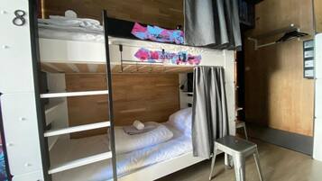 A bunk bed room with a wooden floor, a small stool, and a curtain.