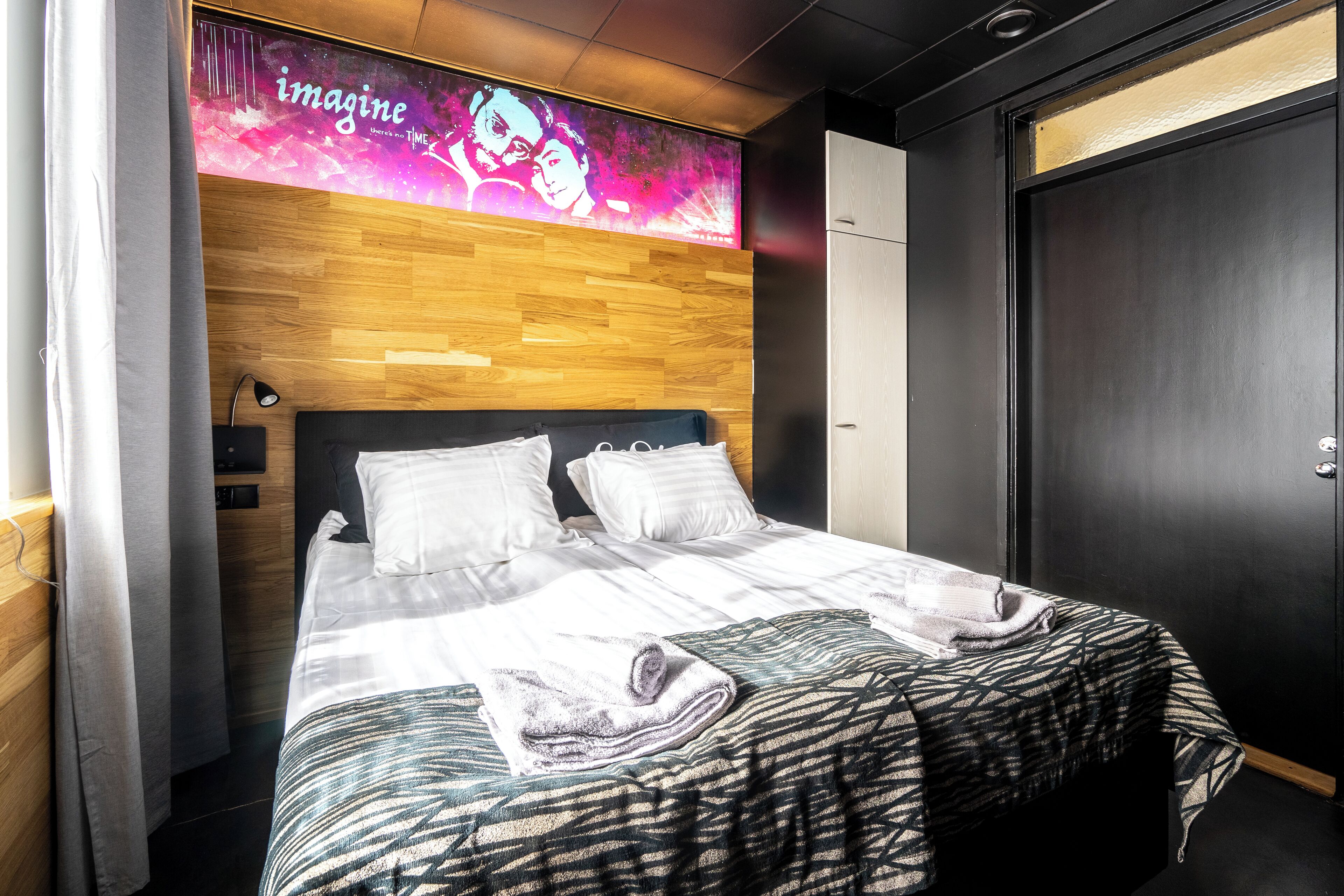 A modern hotel room with a wooden headboard, a large bed with white linens, and a digital display above the bed.