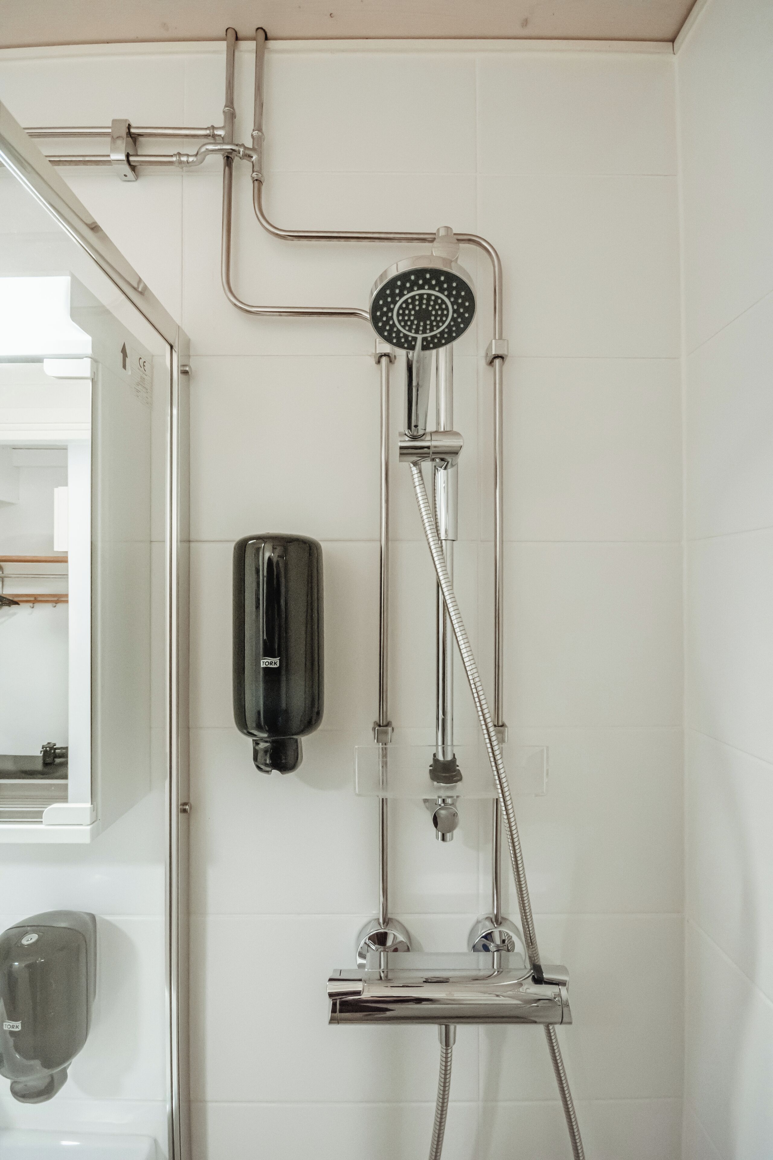 Een douche met een handdouche en een zeepdispenser die aan de muur is bevestigd.