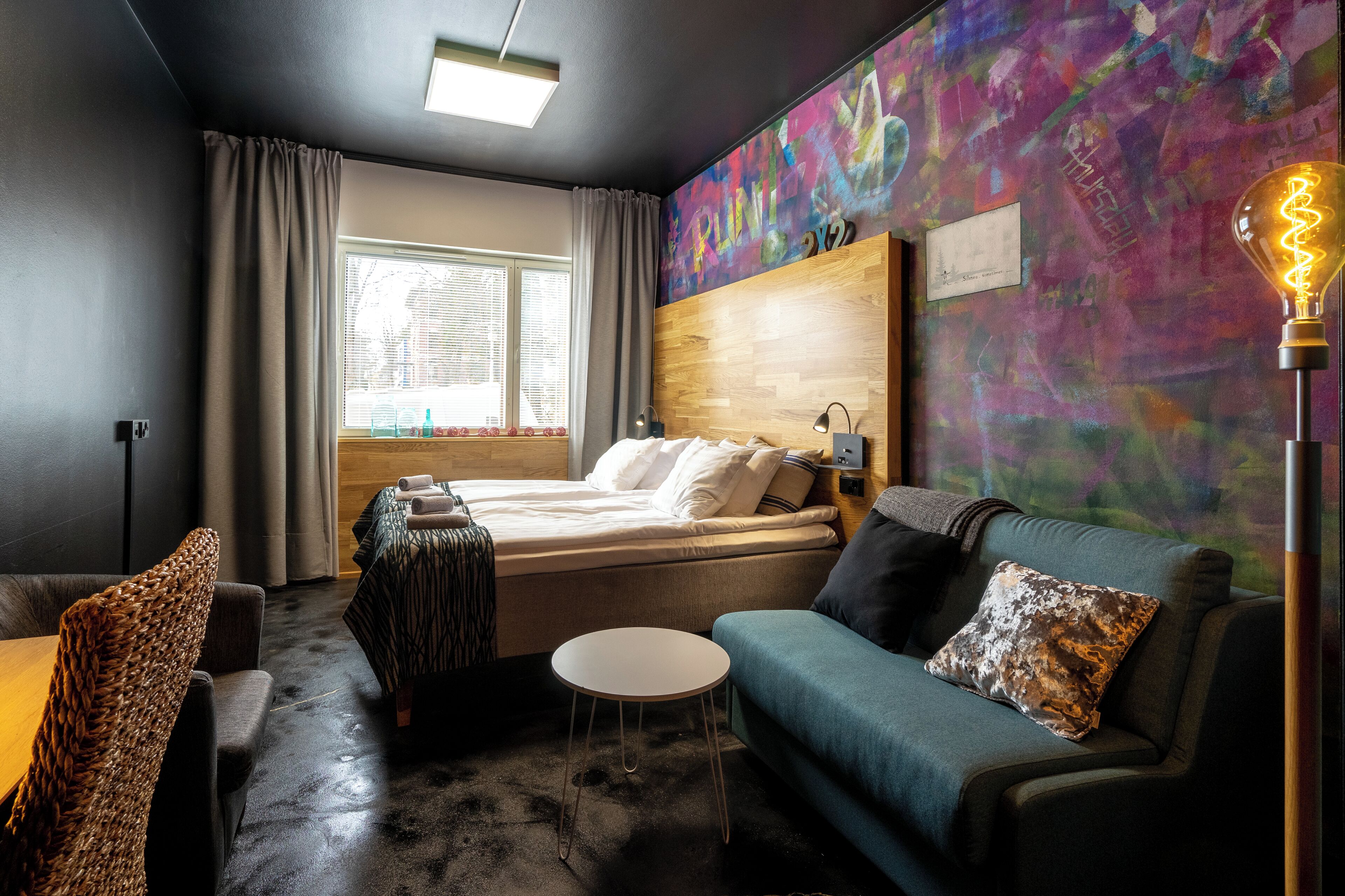 A modern hotel room with a bed, a sofa, a small table, and a lamp.