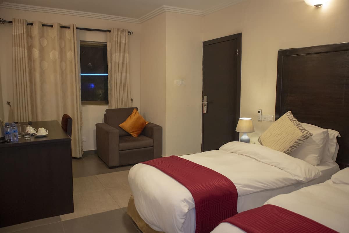 A hotel room with a bed, a chair, a desk, and a window with curtains.