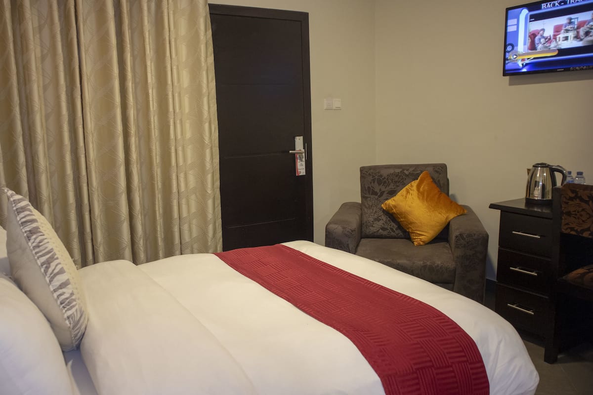 A hotel room with a bed, a chair, a desk, and a television.