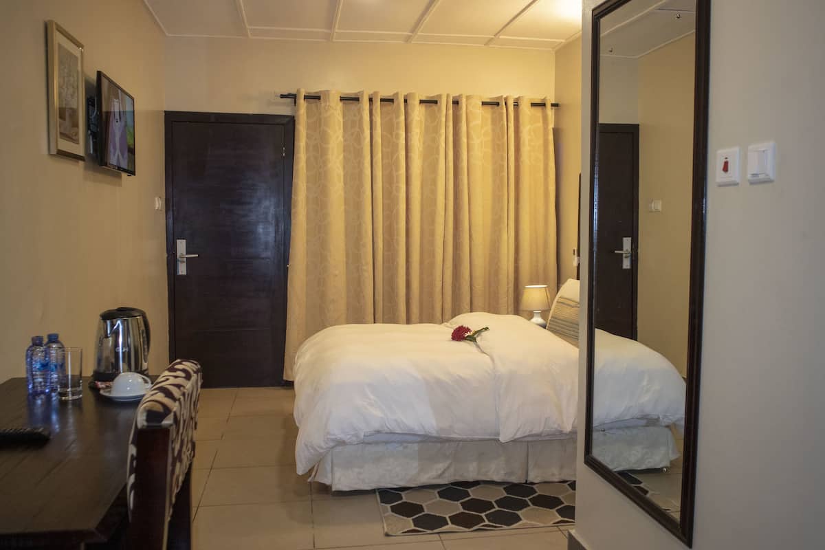 A hotel room with a bed, a desk with a chair, a coffee maker, and a mirror.