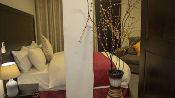 Ein Hotelzimmer mit einem Bett, einer Nachttischlampe, einer Vase mit Zweigen und einem Sofa im Hintergrund.