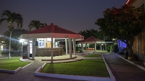 Un espacio exterior bien iluminado con una zona de estar cubierta, un bar y un pequeño jardín.