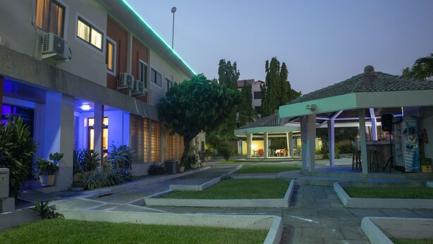 Un patio de hotel con zona de estar cubierta, iluminación exterior y césped bien cuidado.