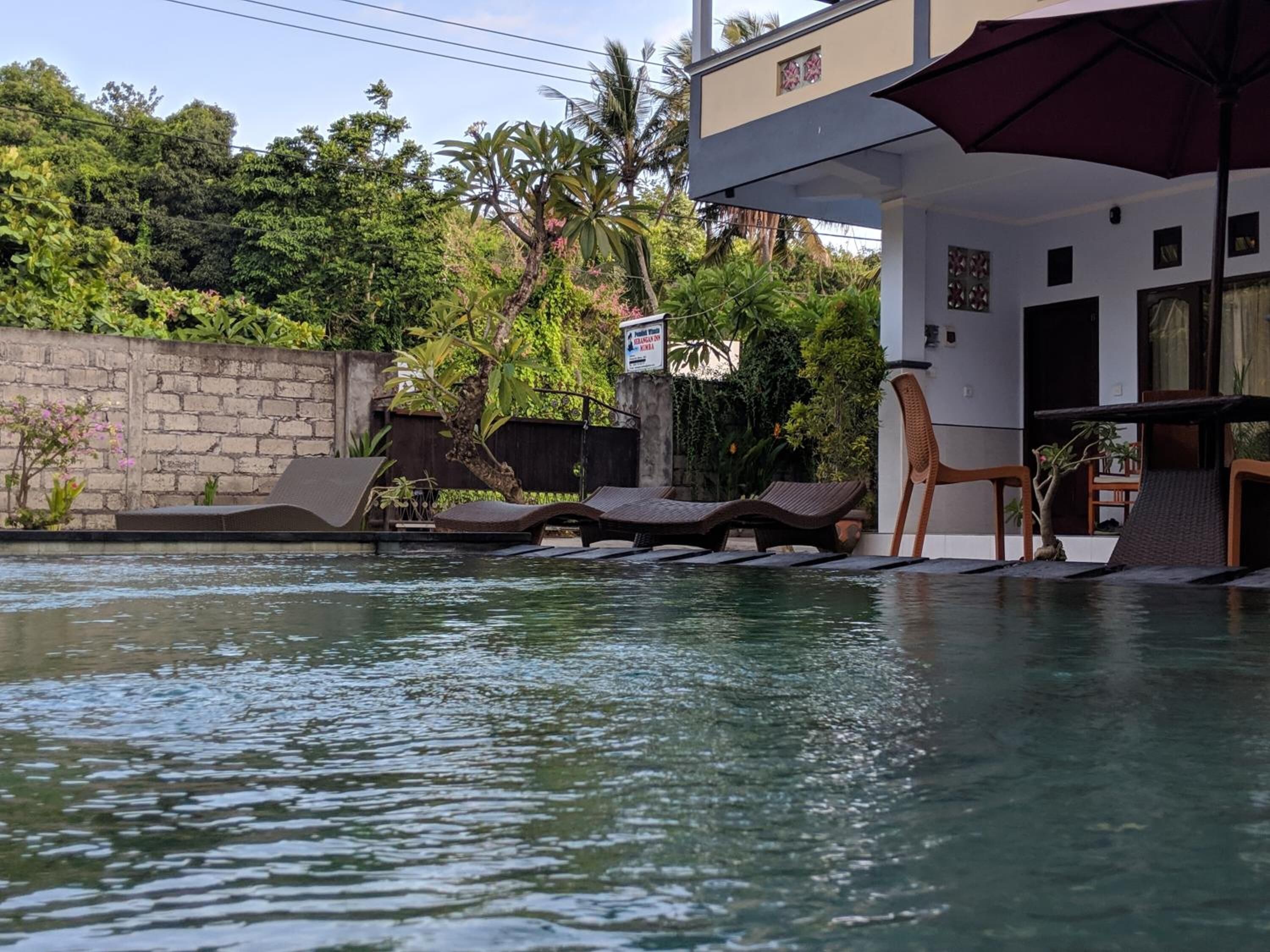 A pool area with lounge chairs and a table, surrounded by lush greenery and a stone wall.