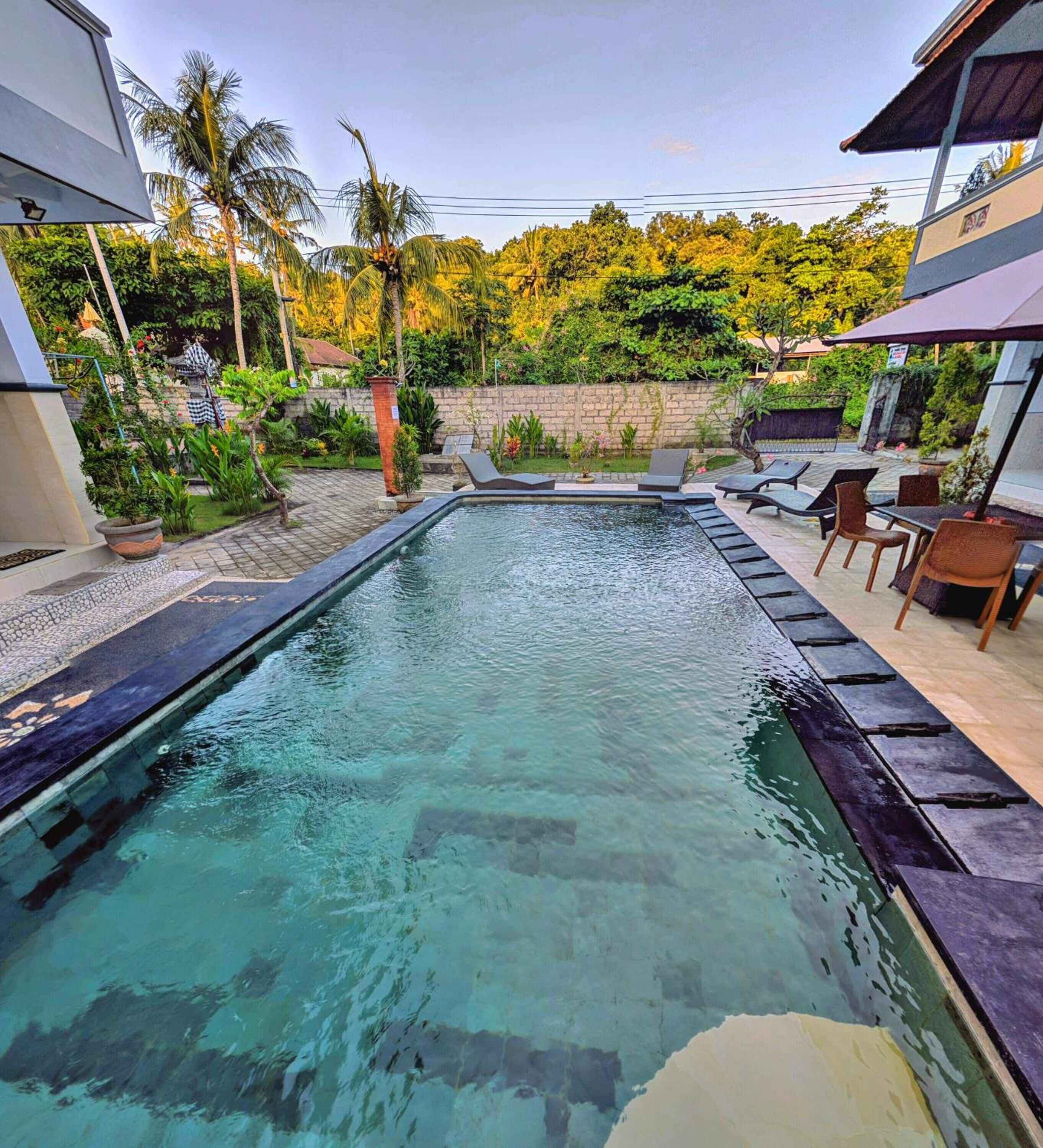 A rectangular swimming pool with clear water, surrounded by a tiled deck and outdoor furniture.