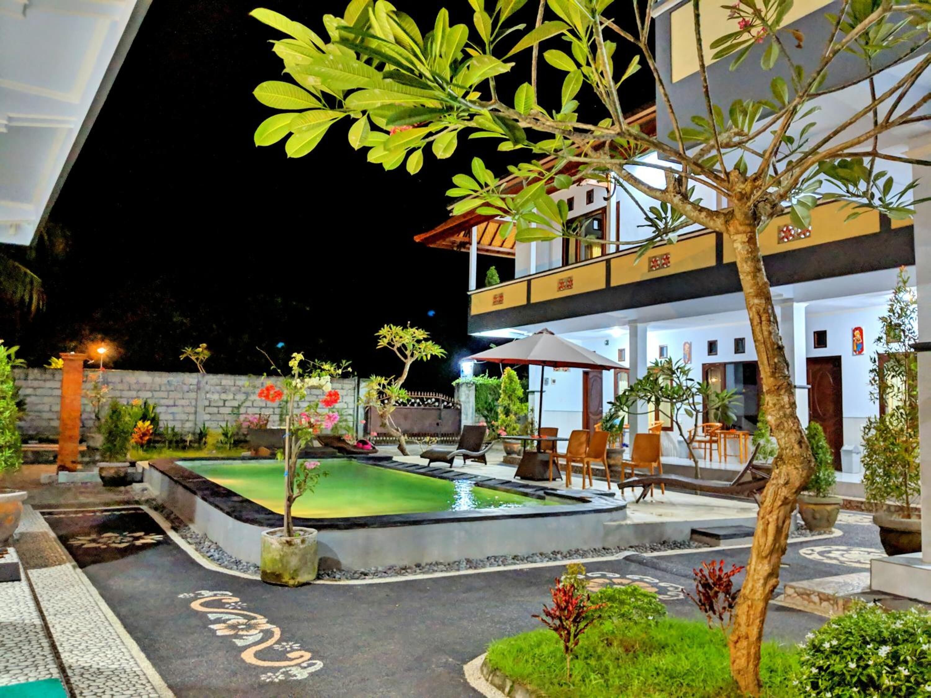 Un patio con piscina, mobiliario de exterior y un edificio de dos pisos con balcones.