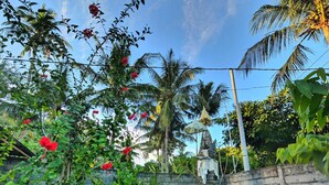 A garden pathway leading to a statue, surrounded by lush greenery and flowering plants. - Serangan Inn Mimba (Padangbai)