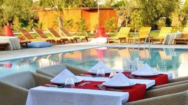 A poolside dining area with tables set for service, lounge chairs, and a pool.