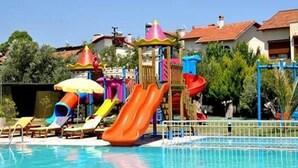 A swimming pool with colorful slides and sun umbrellas, surrounded by lounge chairs and a building in the background.