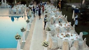 A poolside wedding reception with round tables and white drapery.