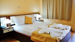 A hotel room with a bed, two bedside tables, a lamp, and a window with curtains.