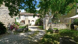 A courtyard with a gravel path leading to a stone building, surrounded by greenery and a white fence. - Ferme Le Grand Cordy (Grignan)