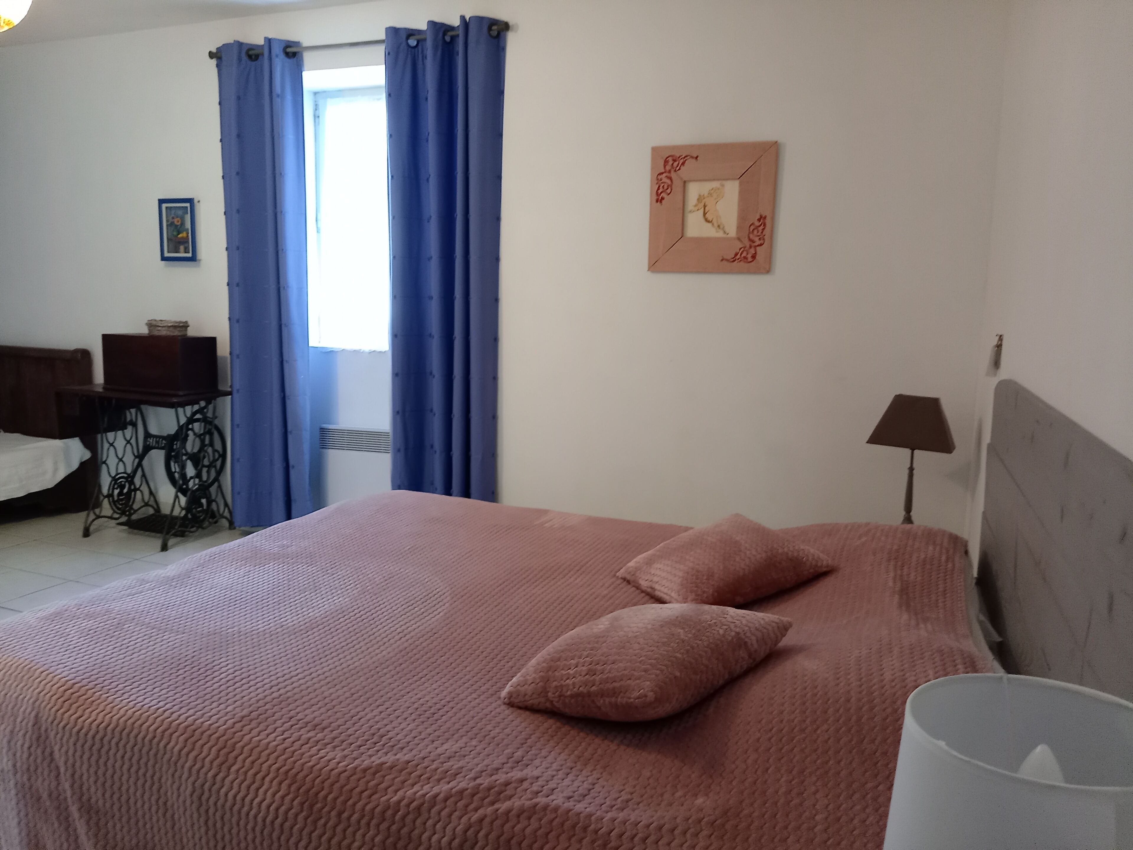 A bedroom with a bed, a desk, a lamp, and a window with blue curtains.