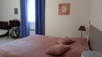 A bedroom with a bed, a desk, a lamp, and a window with blue curtains.