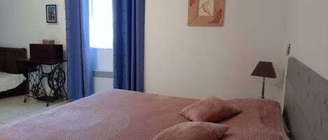 A bedroom with a bed, a desk, a lamp, and a window with blue curtains.