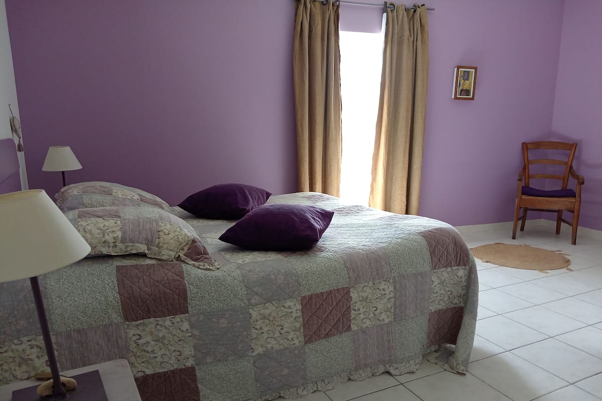 A bedroom with a bed, a chair, a lamp, and a window with curtains.