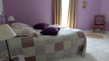 Un dormitorio con cama, una silla, una lámpara y un ventanal con cortinas.