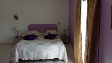 A bedroom with a bed, two bedside lamps, a hanging light fixture, a heart-shaped decoration, and a window with curtains.