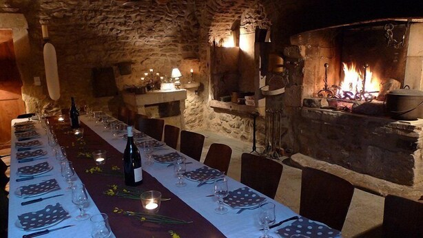 A long dining table set for a meal in a rustic stone-walled room with a fireplace. - Ferme Le Grand Cordy (Grignan)