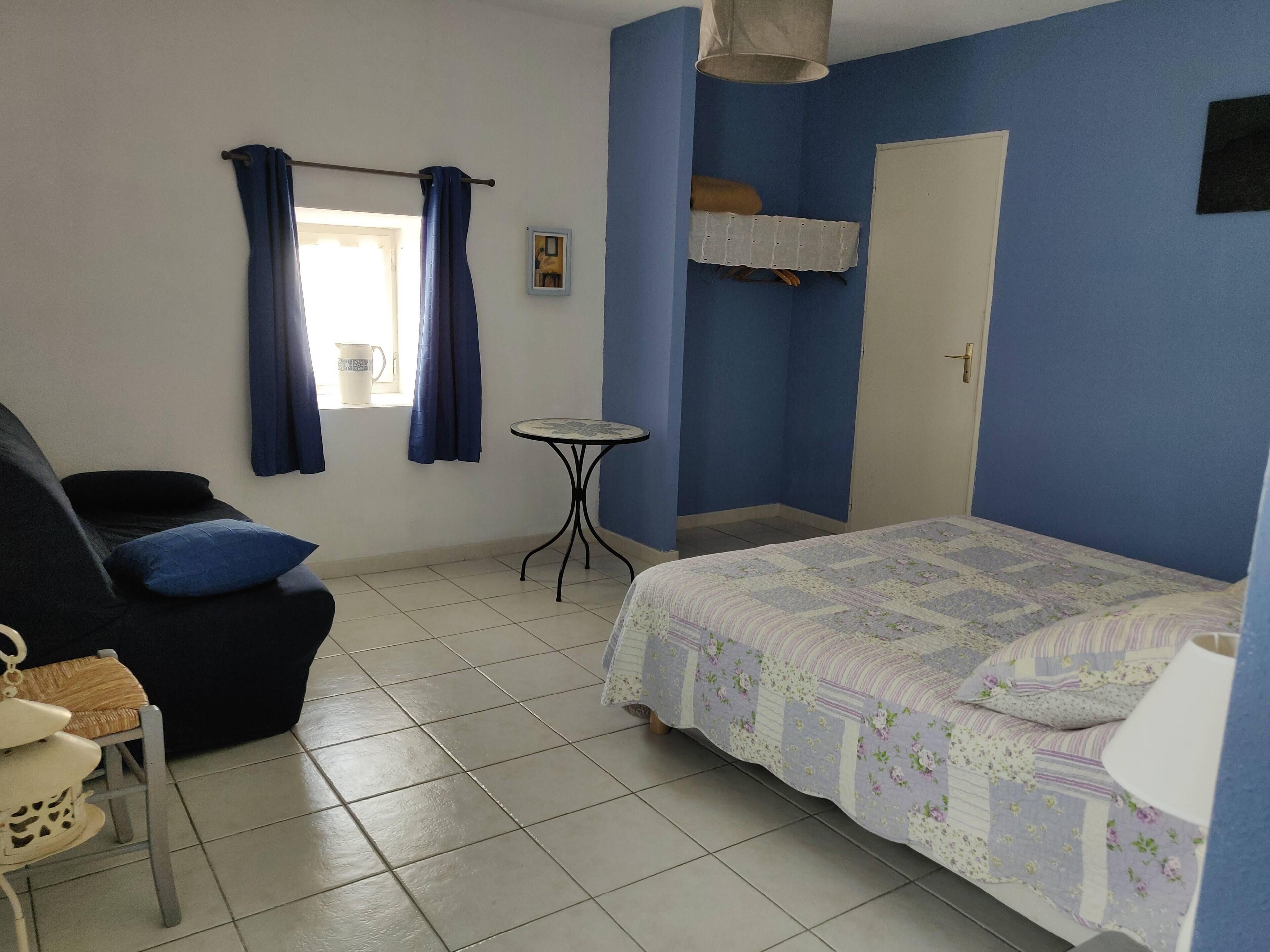 A bedroom with a bed, a chair, a small table, and a window with curtains.