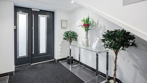 Un hall d’entrée moderne avec un comptoir d’accueil en verre, une porte noire et deux plantes en pot.