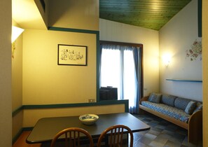 A dining area with a table, chairs, a bowl, a framed picture, a sofa, and a window with curtains. - Residence Mirelladue (Ponte di Legno)
