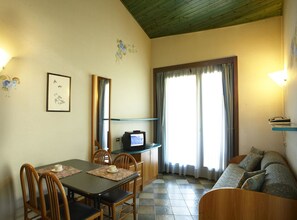 A cozy living room with a dining table, chairs, a sofa, a television, and a window with curtains. - Residence Mirelladue (Ponte di Legno)