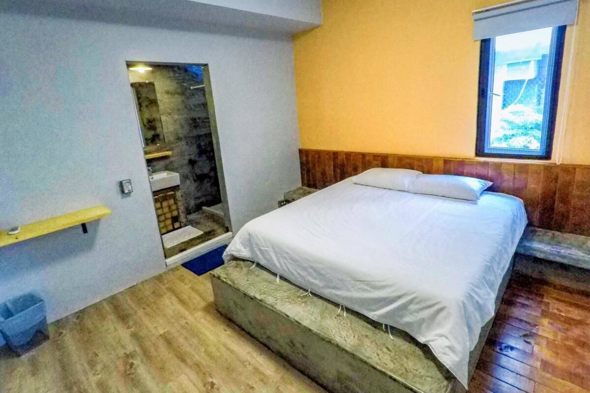 A bedroom with a bed, a small window, and a wooden floor.