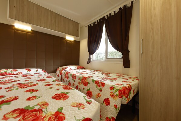 Quarto com duas camas, cabeceira de madeira e janela com cortinas.