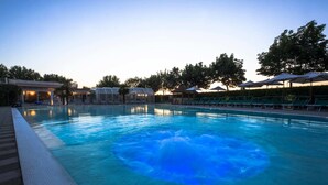 Una piscina con sillas de descanso y sombrillas, rodeada de árboles y edificios.